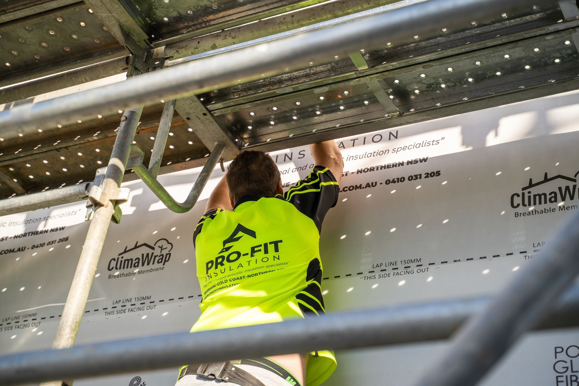 Person in yellow safety vest installing building material on a structure using scaffolding.