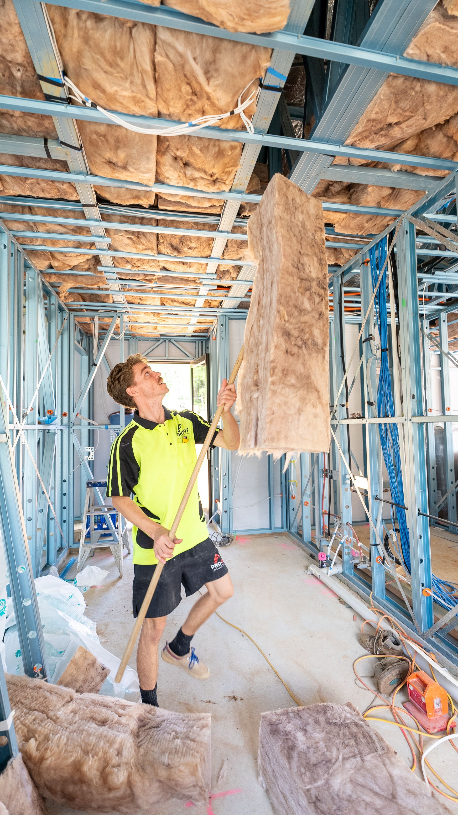 Construction worker installing insulation in a new building, holding a large rectangular piece above his head.