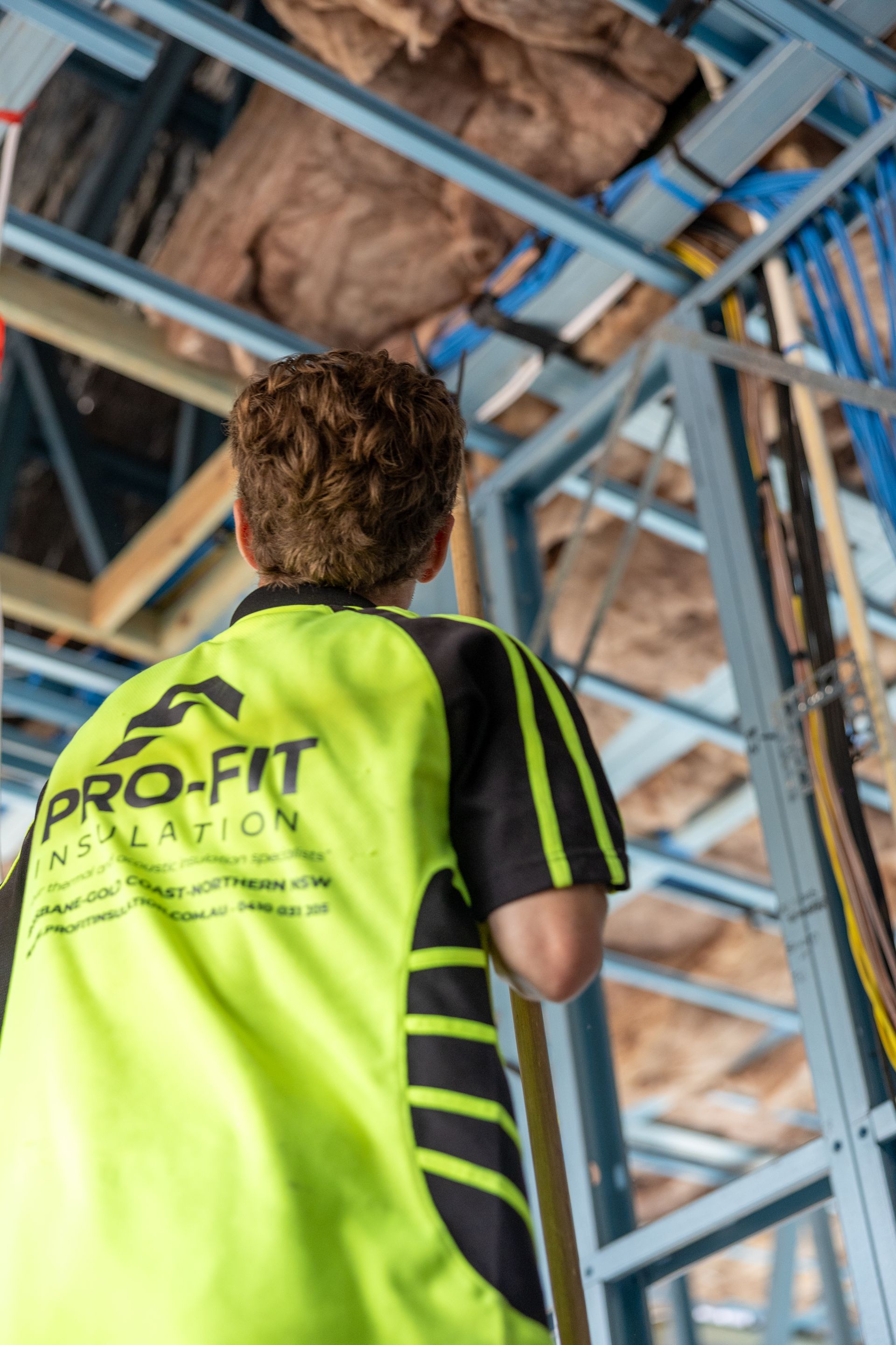 Construction worker in a lime green shirt with tool belt, drilling into wooden ceiling beams.
