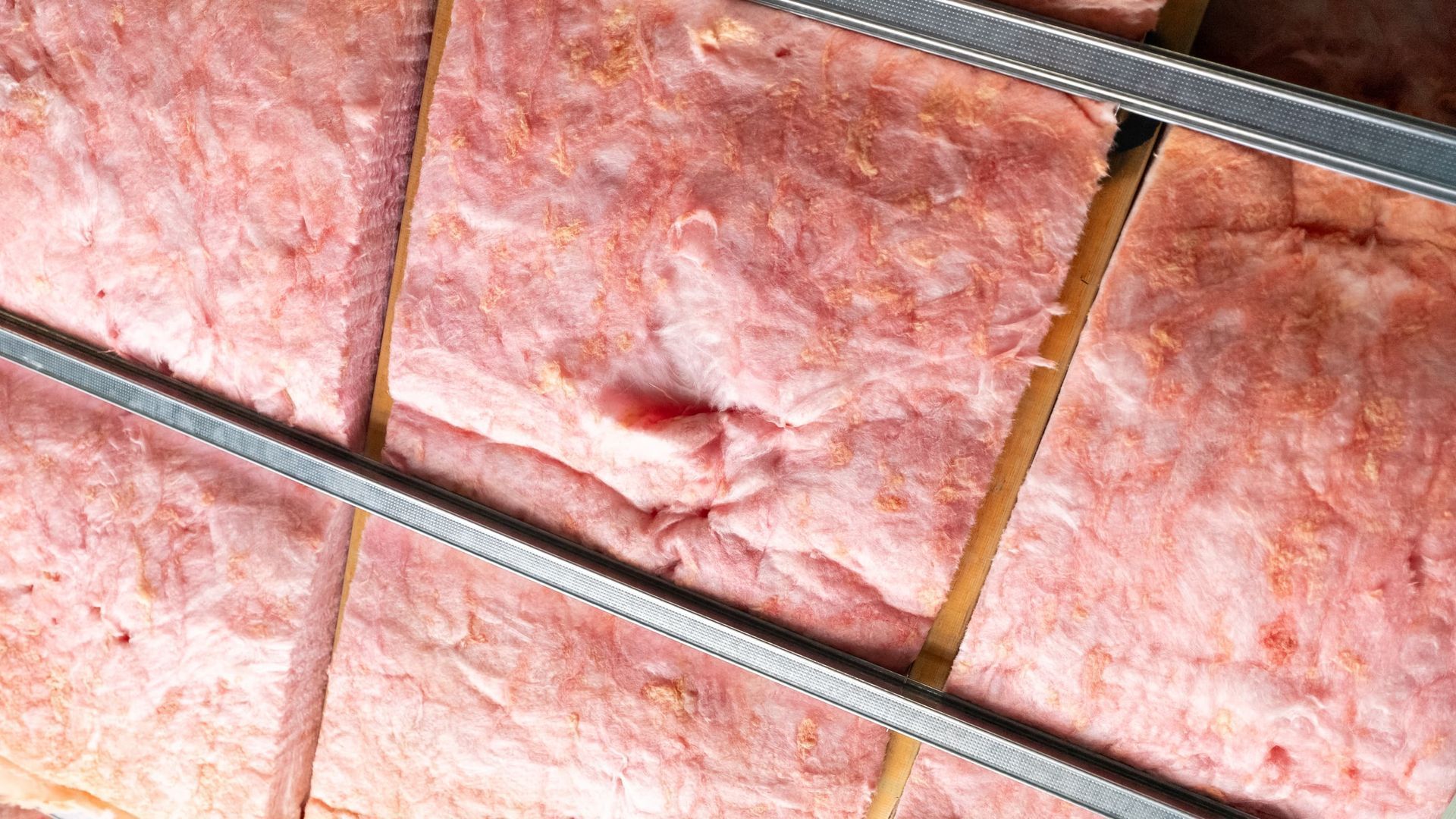 Pink fiberglass insulation installed between metal studs.