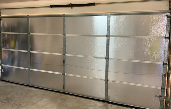 Garage door, shiny silver with horizontal panels, set in a concrete garage.