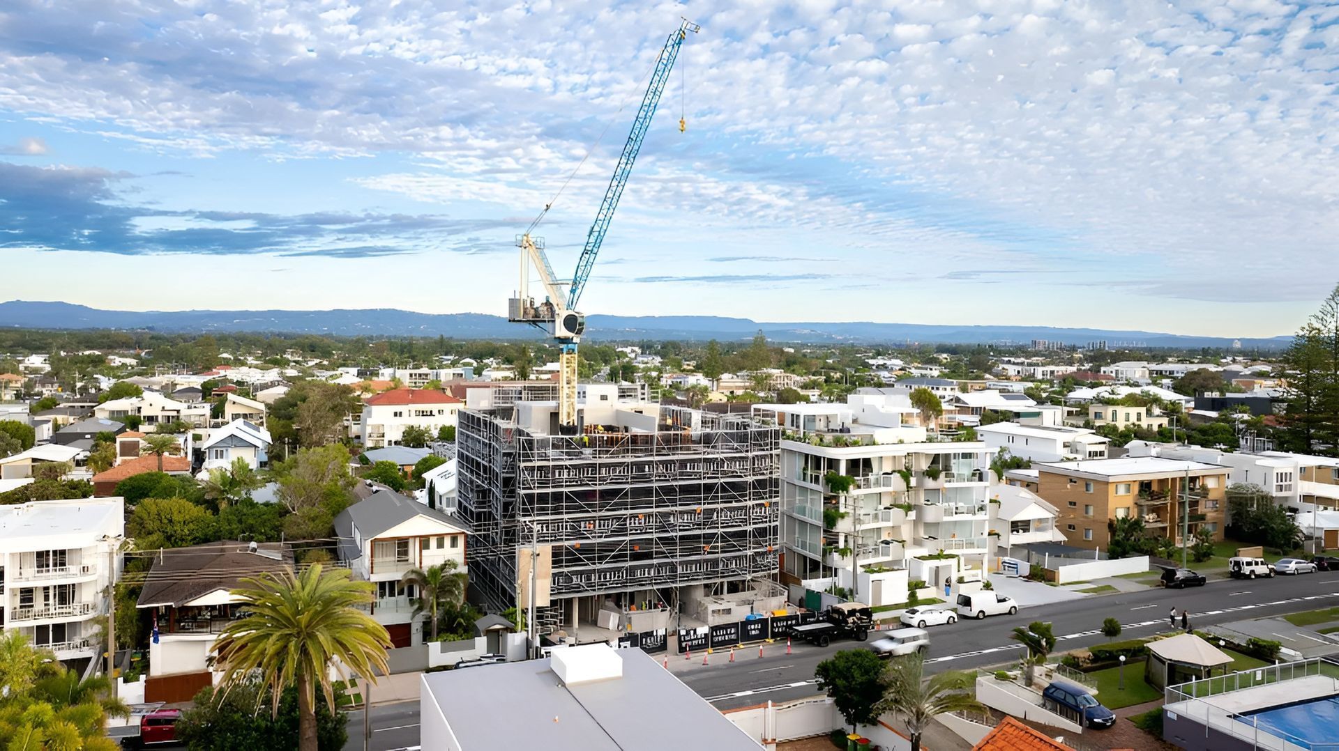 Construction site with crane overlooking a town with white buildings and a blue sky.