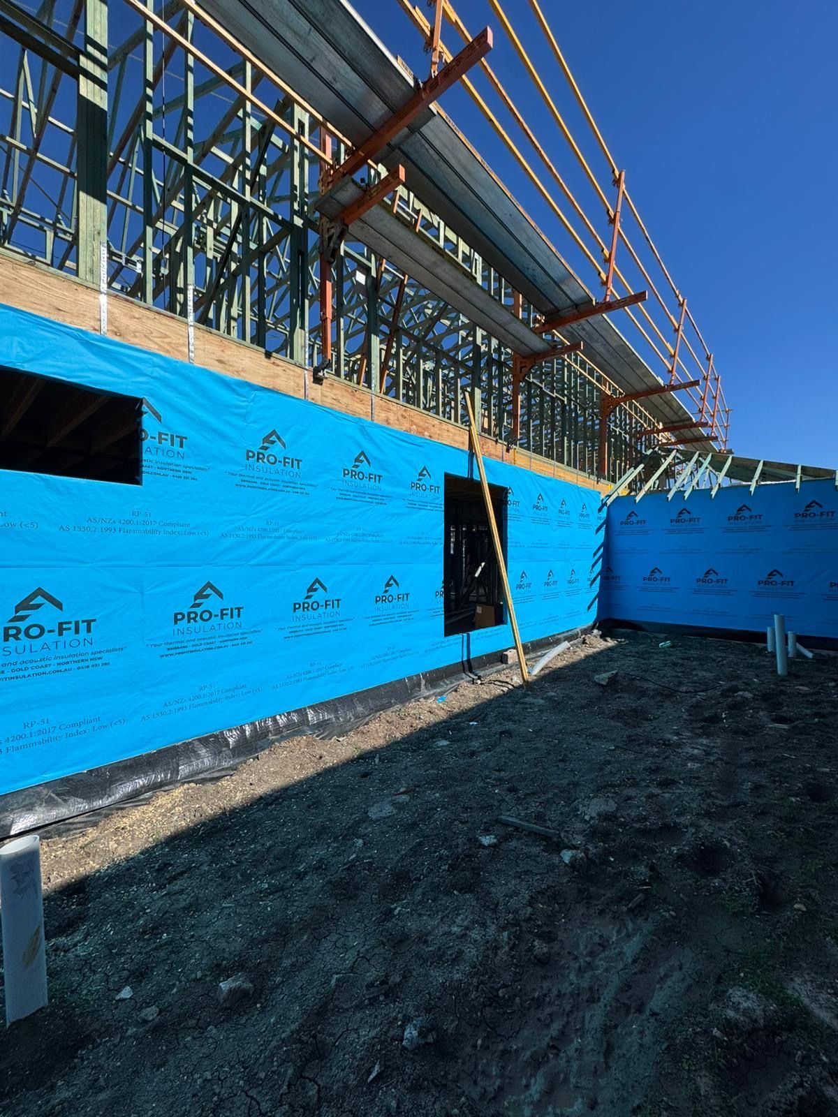 Construction site with blue protective wrap on a building's exterior, against a clear blue sky.