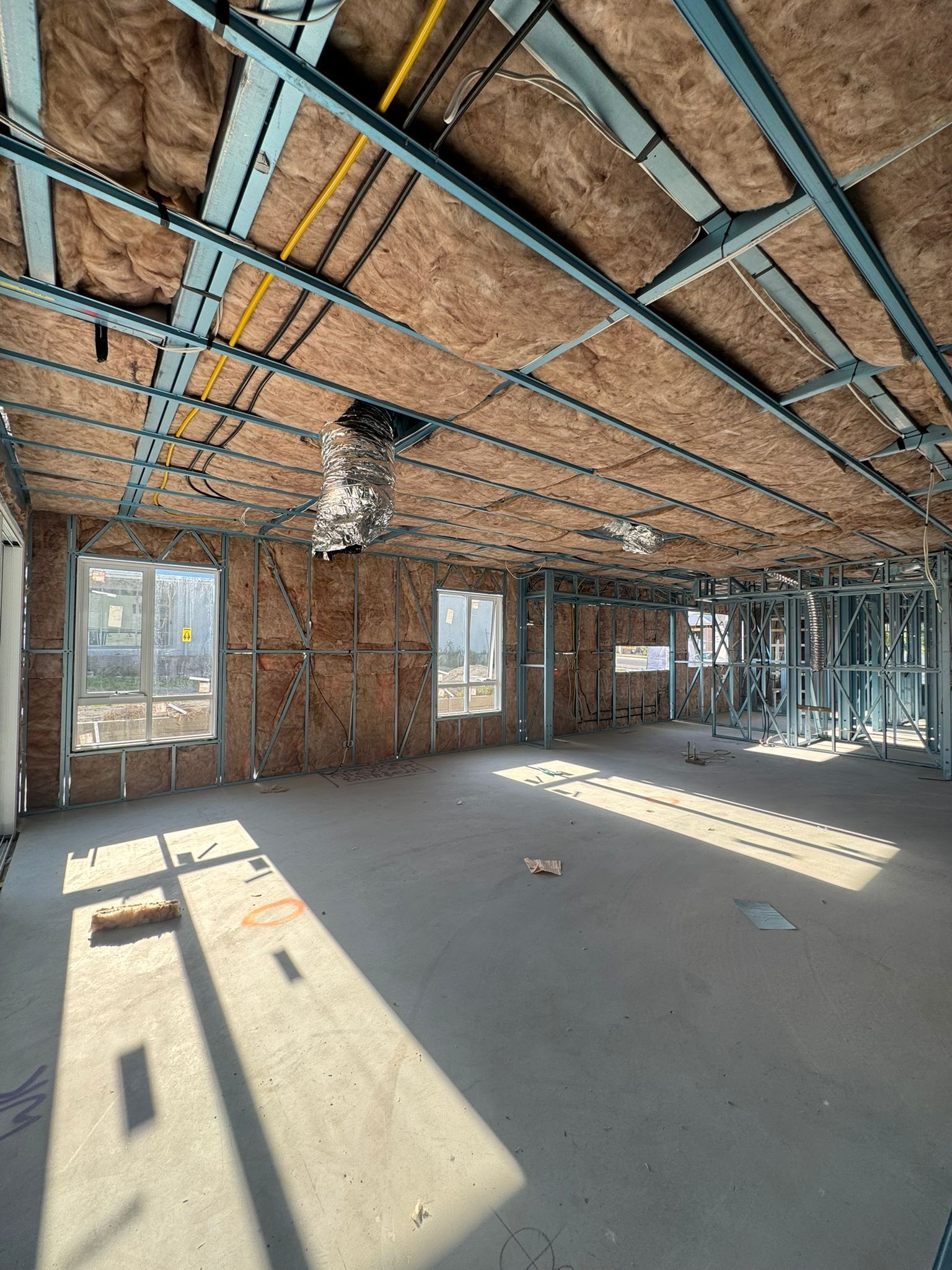 Interior of a building under construction, showing insulated walls, steel framing, and sunlight streaming through windows.