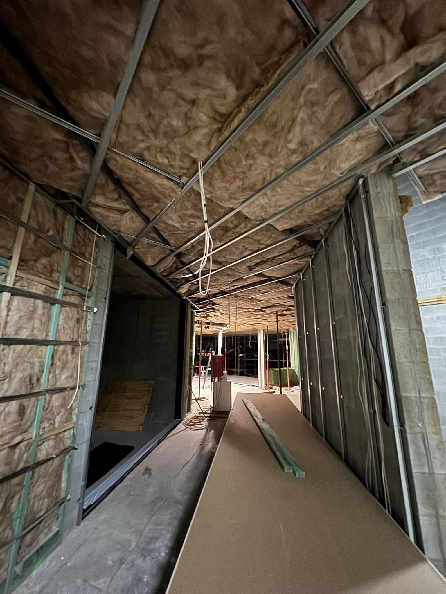 Interior hallway under construction; metal studs, insulation, and drywall visible.
