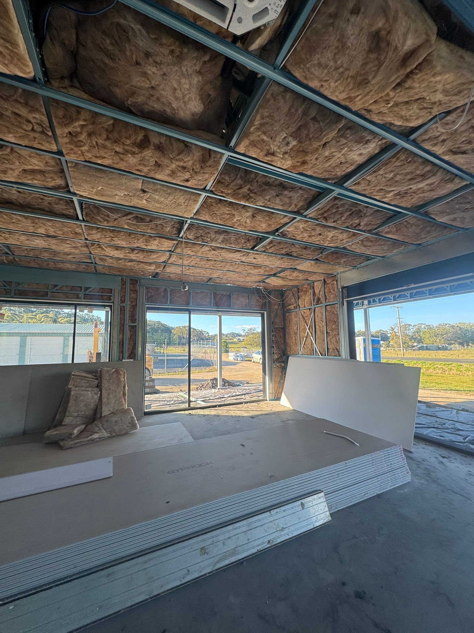Interior view of a room under construction, showing insulation, metal framing, and drywall.