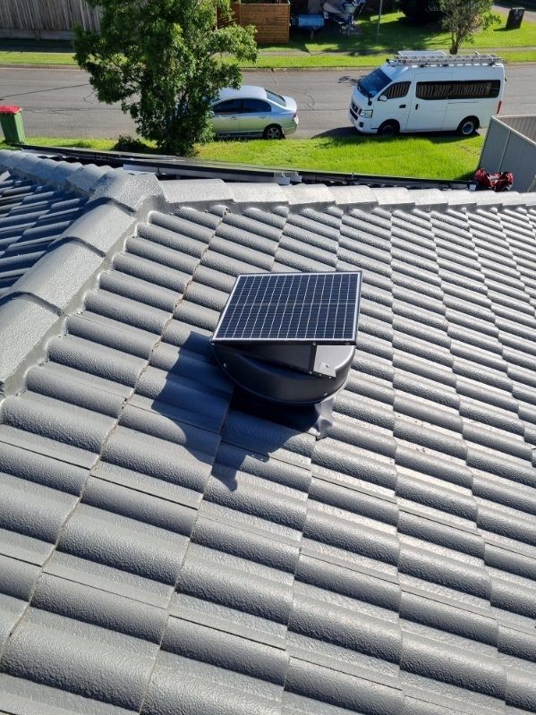 Solar roof vent on gray tiled roof. Cars and a van are in the background on the street.