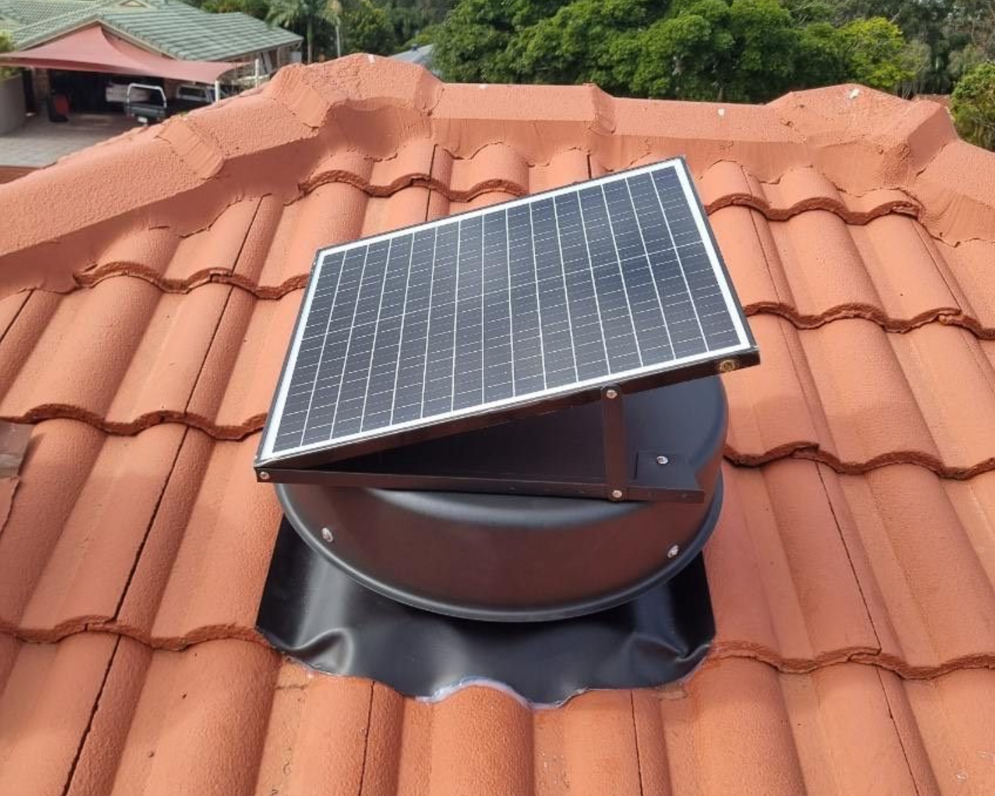 Solar-powered roof vent installed on red tiled roof. The vent has a black base and a solar panel.