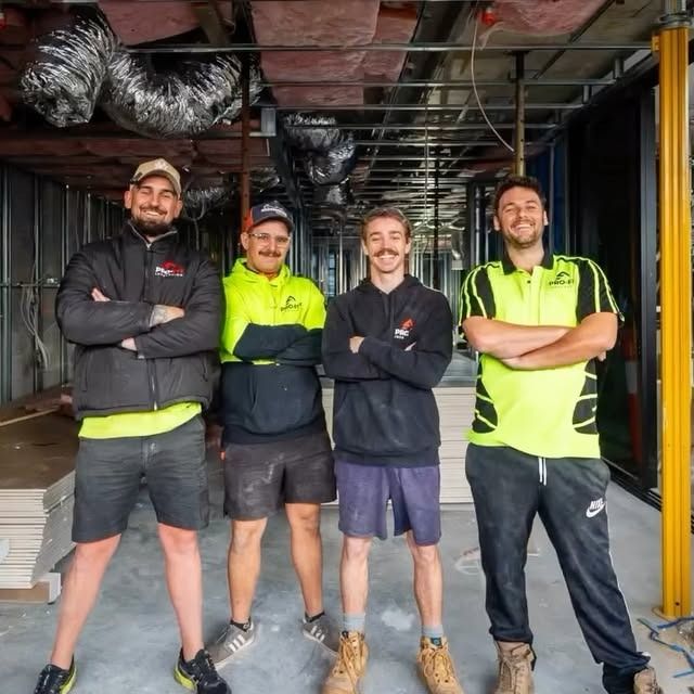 Four construction workers stand in a building under construction, arms crossed, smiling.