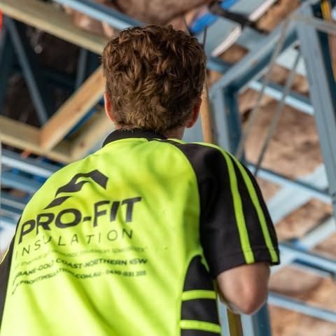 Person wearing a bright yellow Pro-Fit Insulation shirt, inspecting insulation in a ceiling.