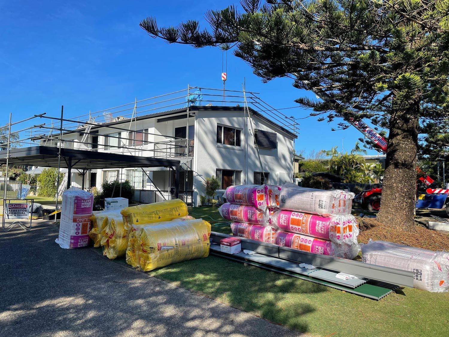 House under construction with insulation materials piled on the lawn. Scaffolding is visible.