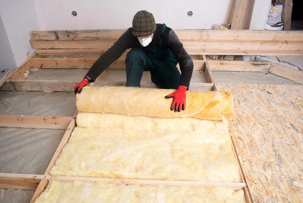 Man installing insulation in a room under construction, wearing gloves, mask, and beanie.