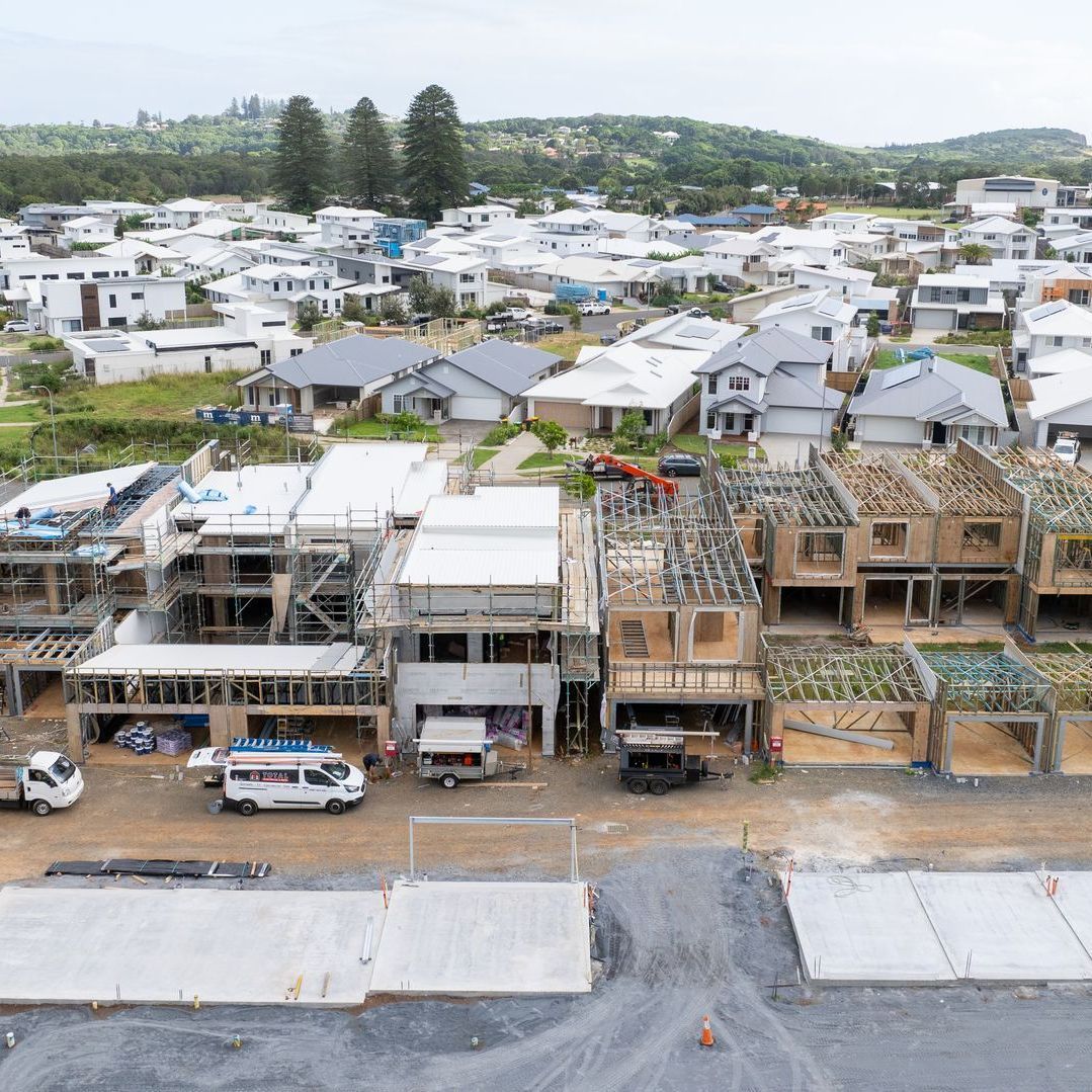 Row of townhouses under construction; completed houses in background; cloudy day.