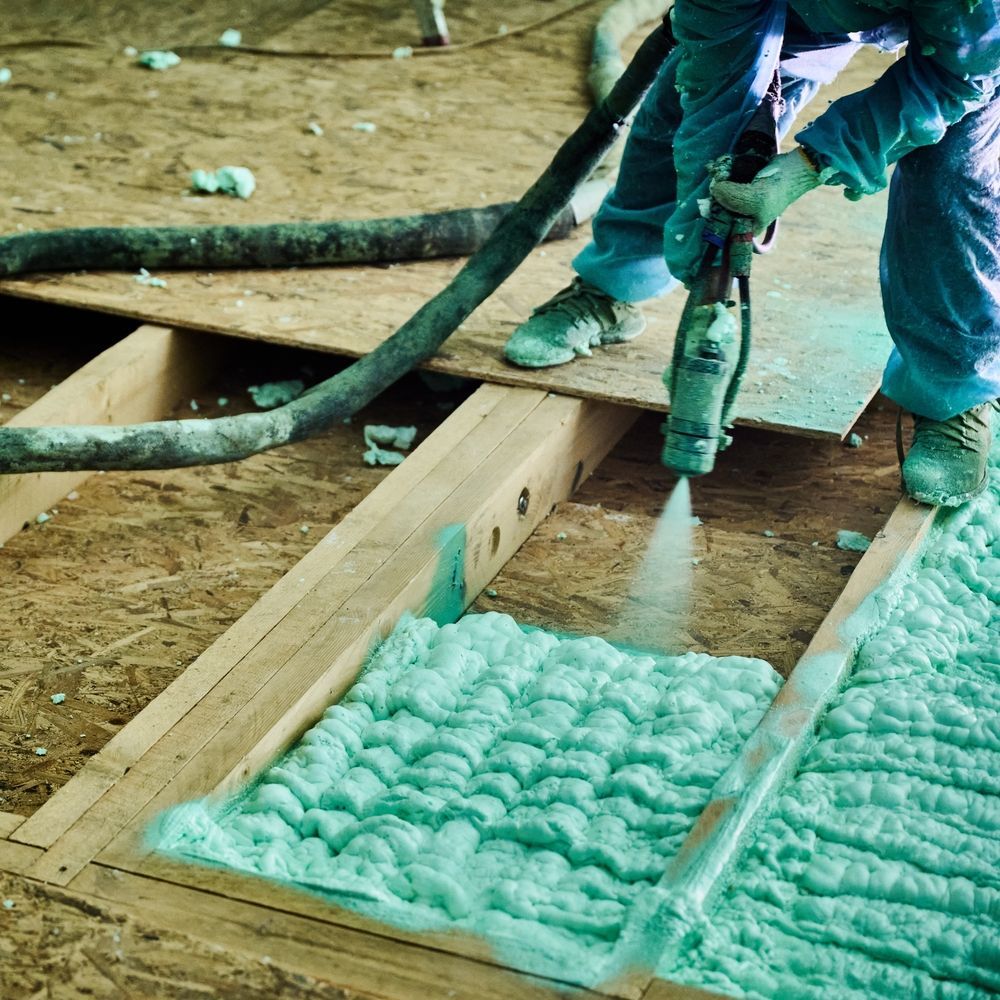 Man spraying green spray foam insulation between floor joists.