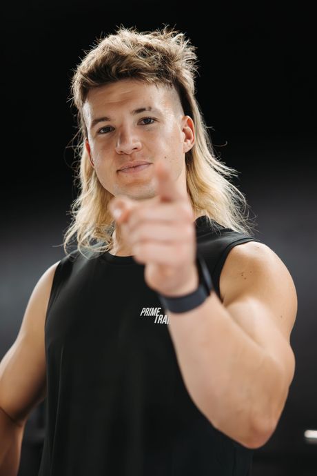 A man with a mullet is pointing at the camera.