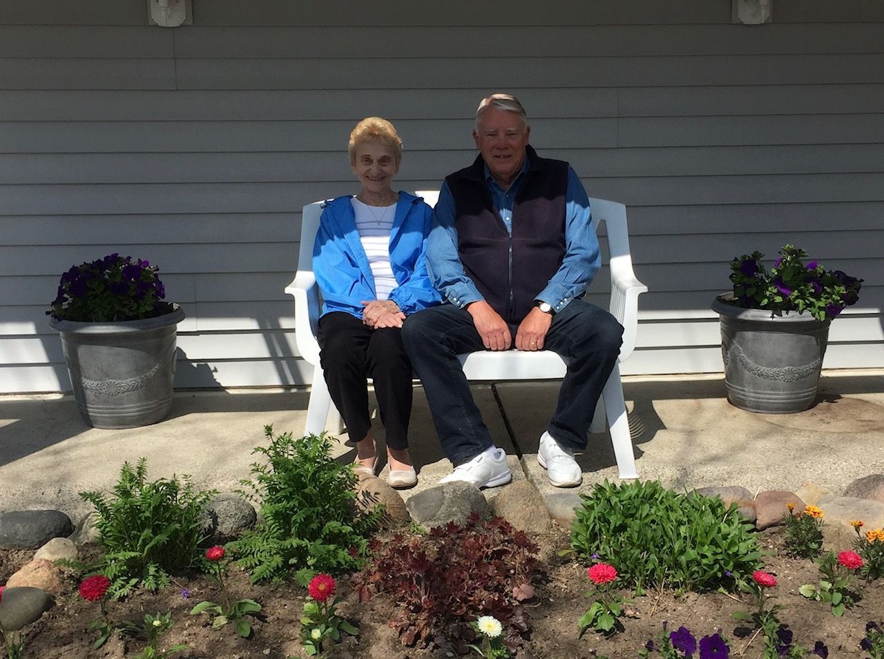 A man and a woman are sitting on a bench in front of a house.