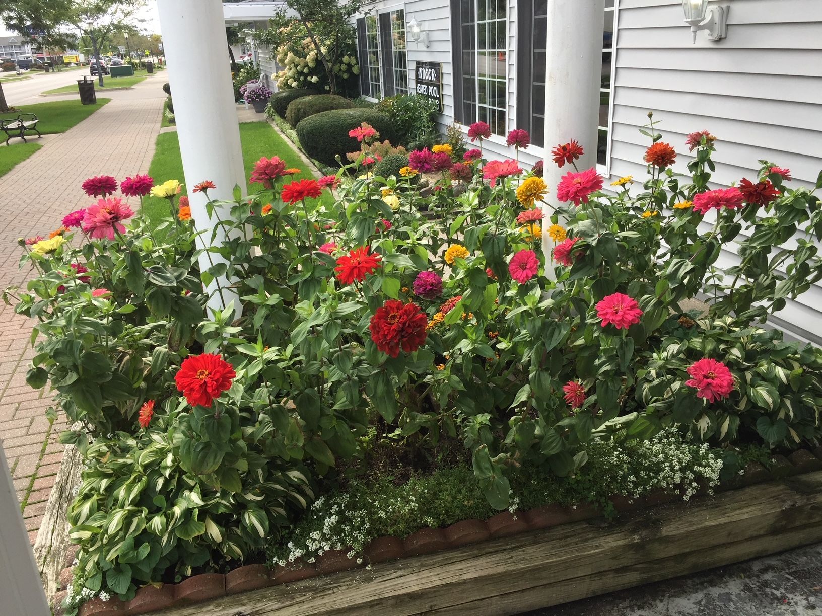A planter filled with colorful flowers is in front of a house.