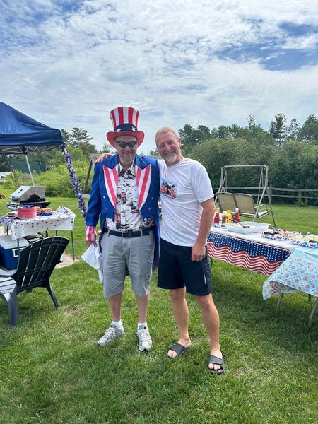 Two men are standing next to each other in a grassy field . one of the men is dressed as uncle sam.