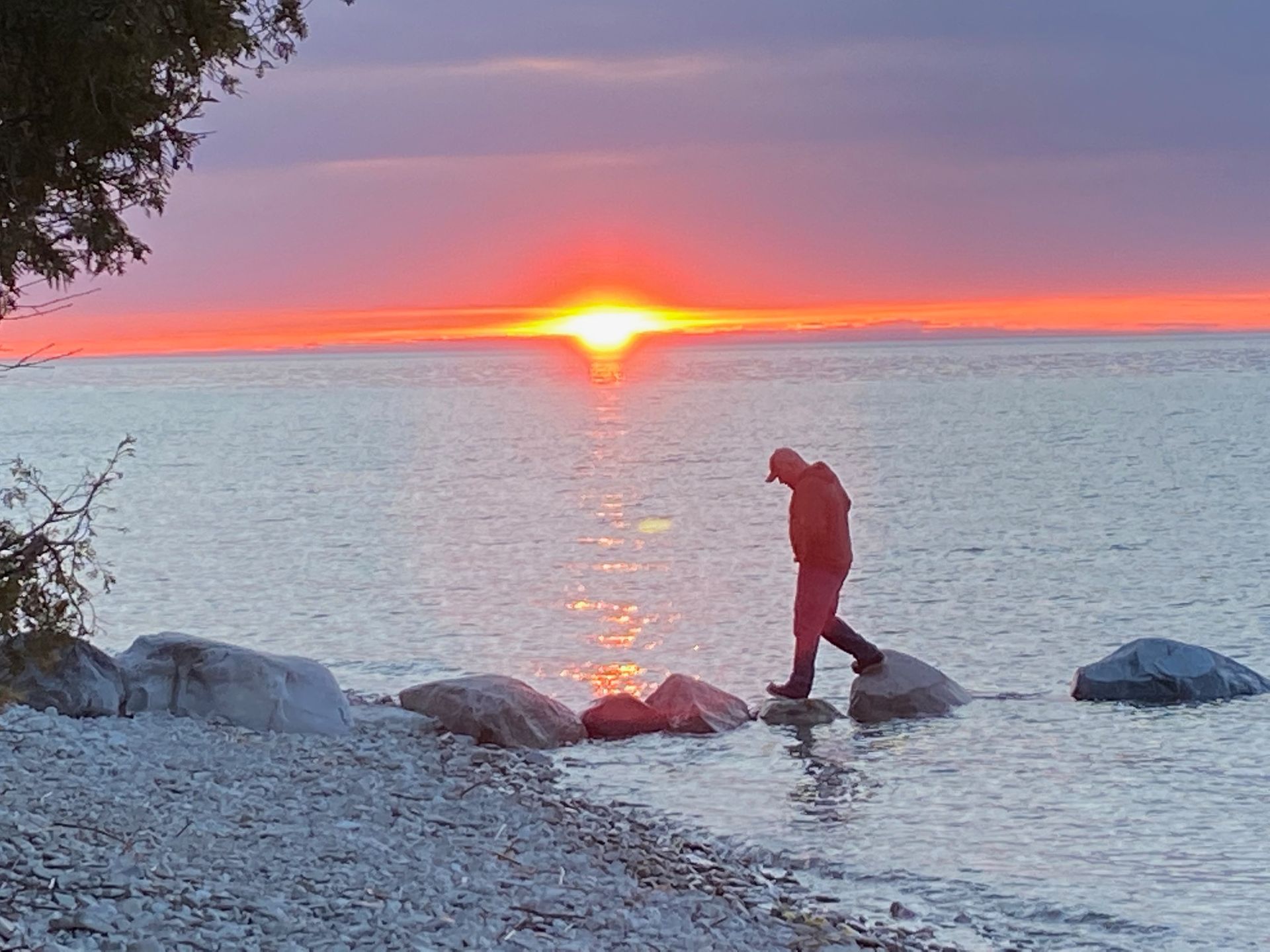 A man walking on a rocky beach at sunset