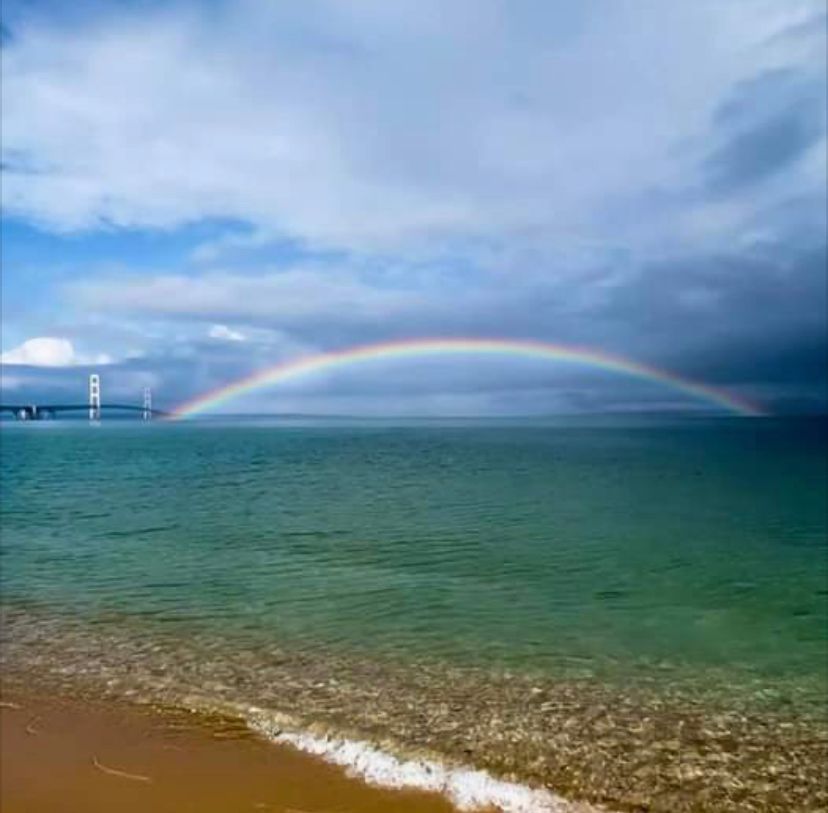 A rainbow over the ocean with a bridge in the background.