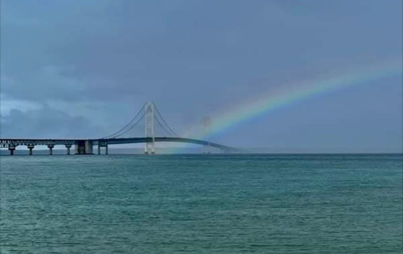 A bridge over a body of water with a rainbow in the sky.