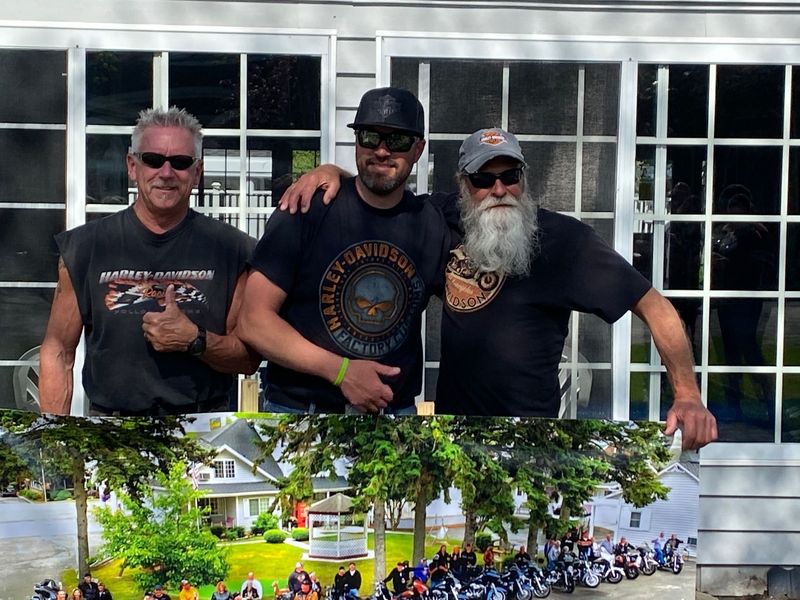 Three men are posing for a picture in front of a house . one of the men is wearing a harley davidson shirt.