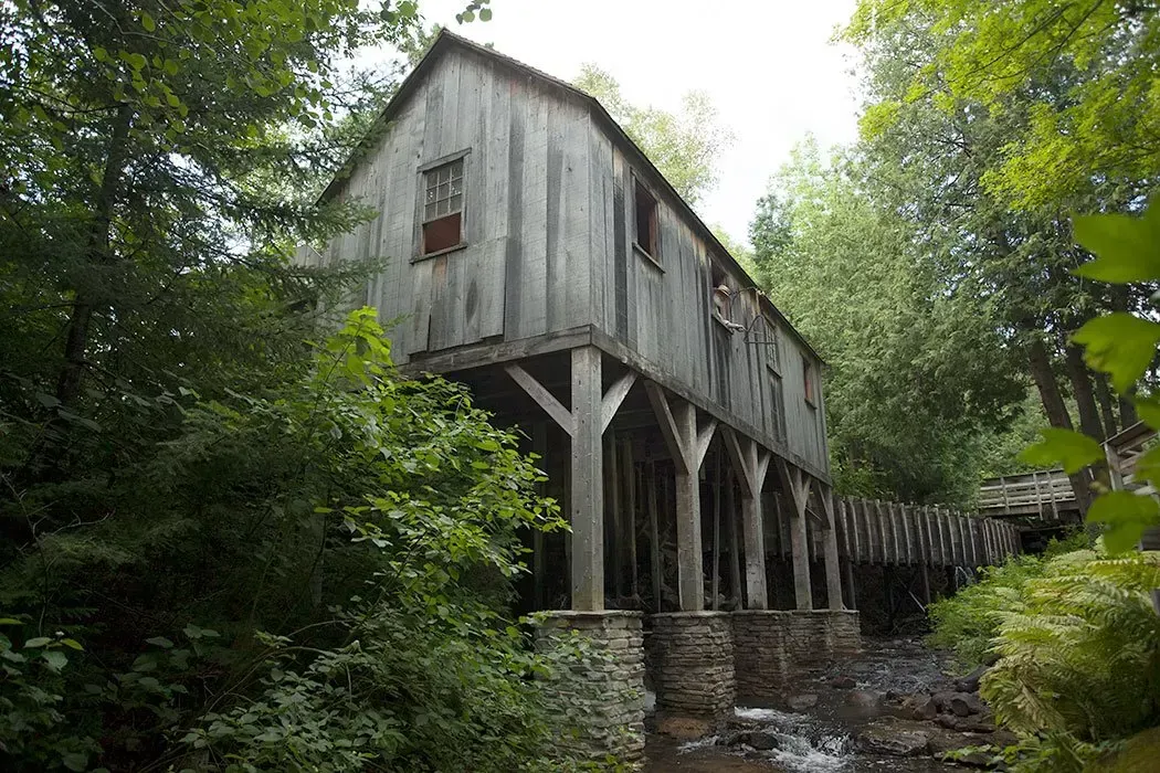 An old wooden bridge over a river in the woods surrounded by trees.