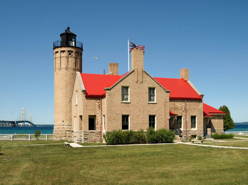 A lighthouse with a red roof and a bridge in the background