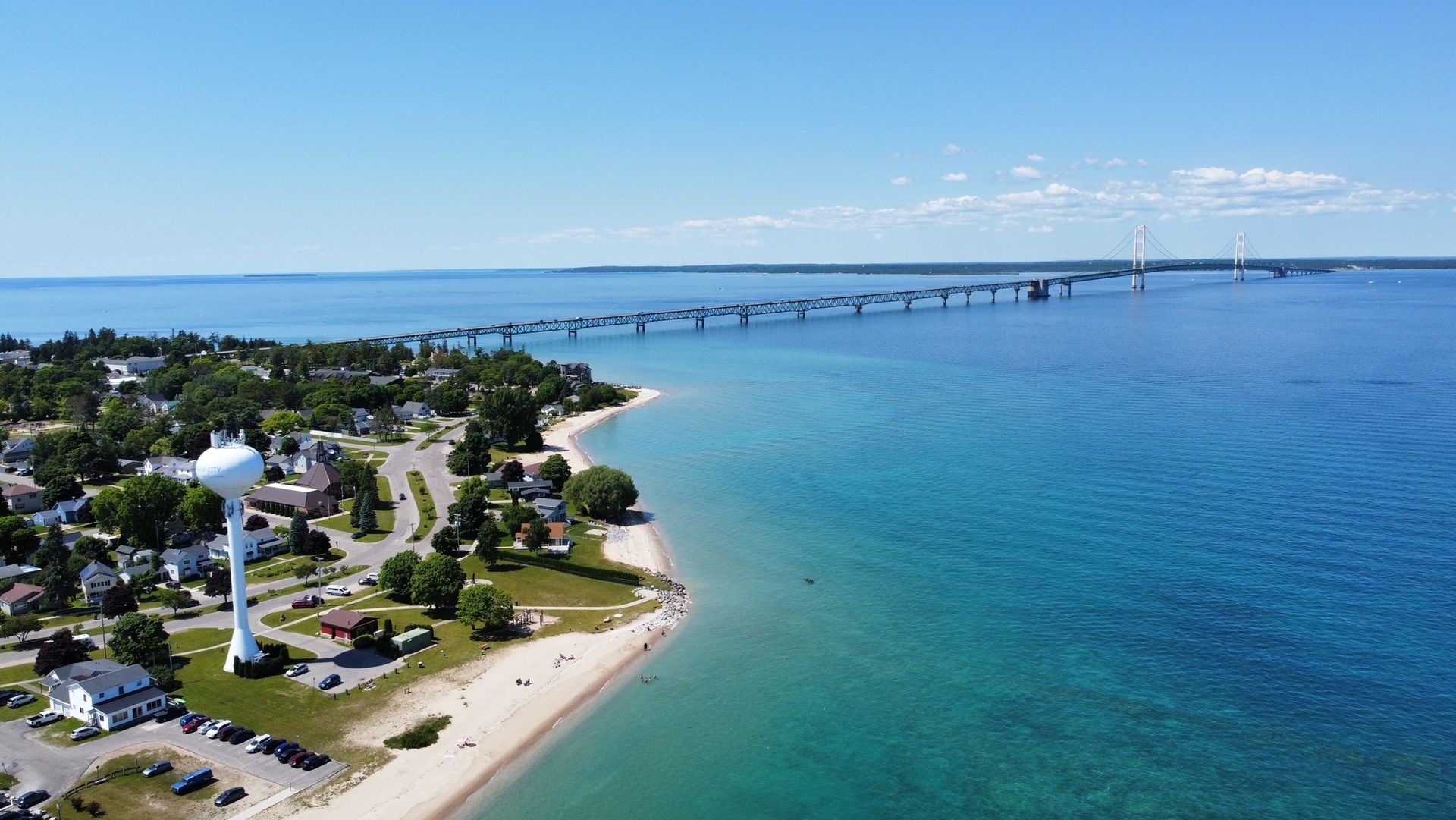 An aerial view of a beach with a water tower and a bridge in the background.