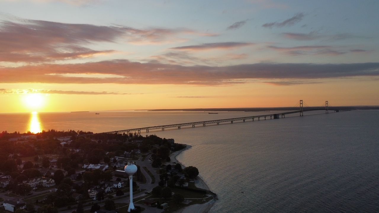 An aerial view of a sunset over a body of water with a bridge in the distance.