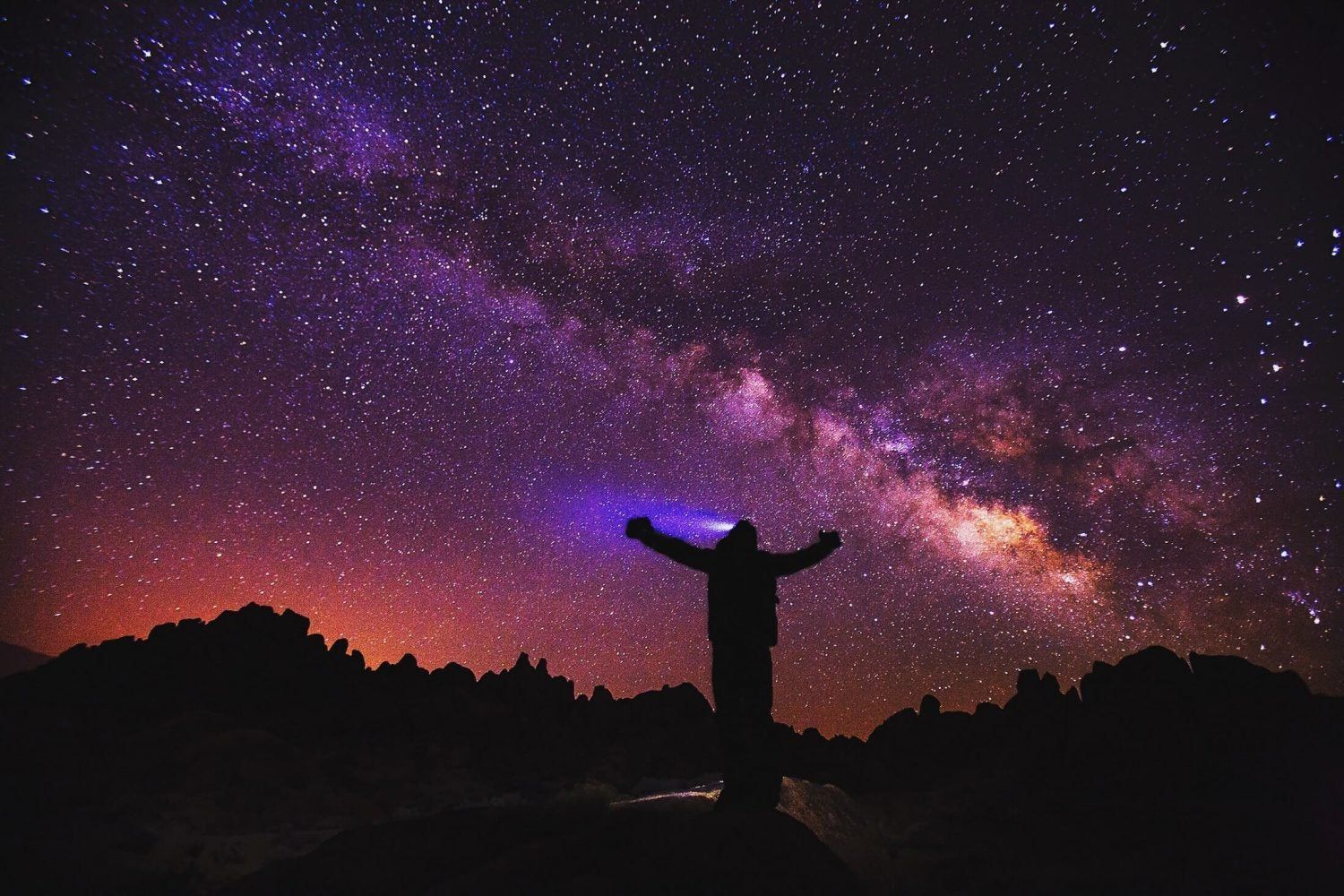 A person is standing under a starry sky with their arms outstretched.