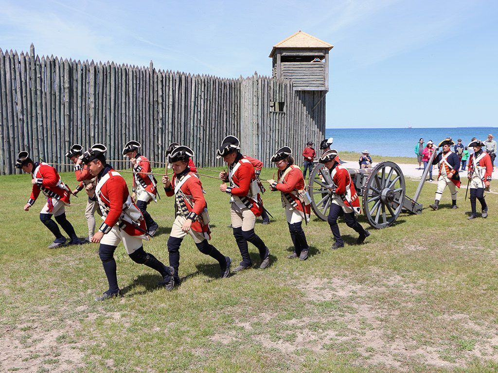 A group of men in military uniforms are marching in front of a cannon.