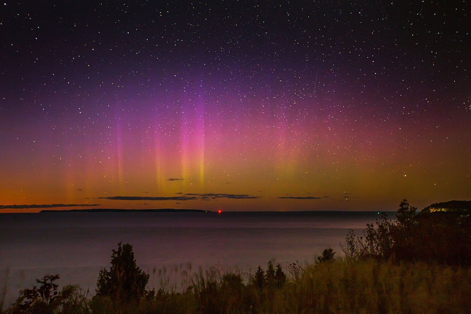 The aurora borealis is visible over the ocean at night.