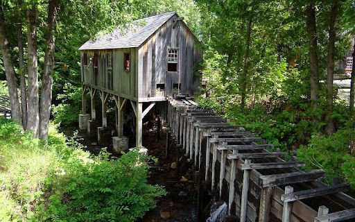 A wooden house is sitting on top of a wooden bridge in the middle of a forest.