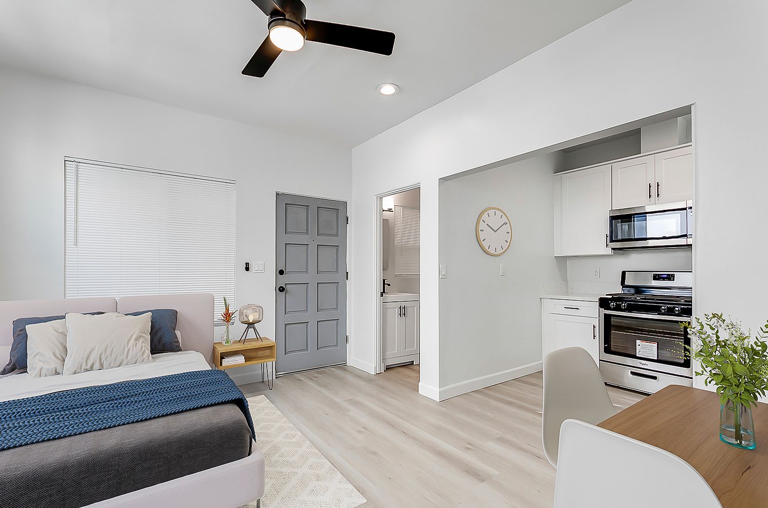 A bedroom with a ceiling fan and a kitchen with a clock on the wall.