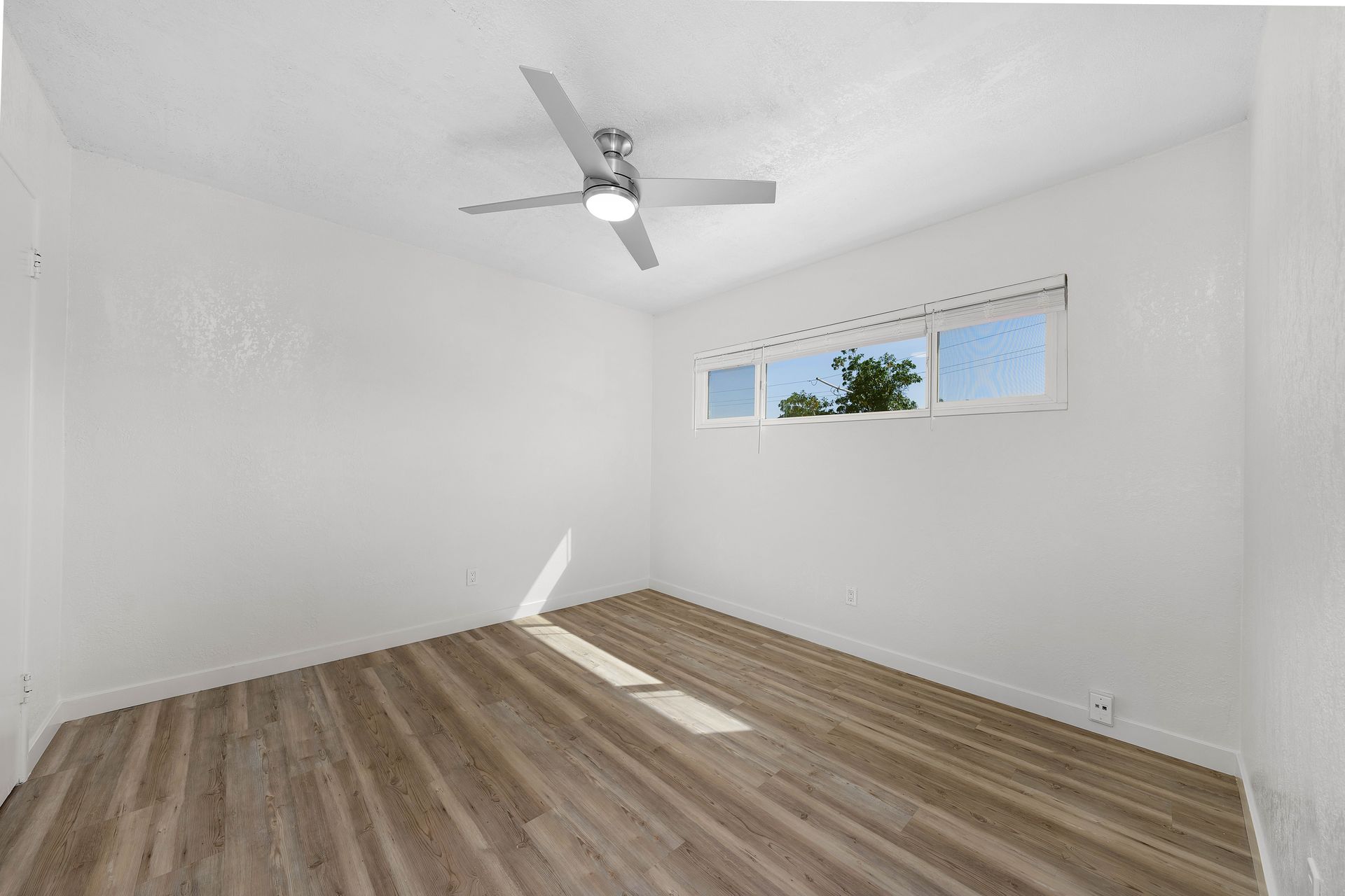 An empty bedroom with a ceiling fan and a window.