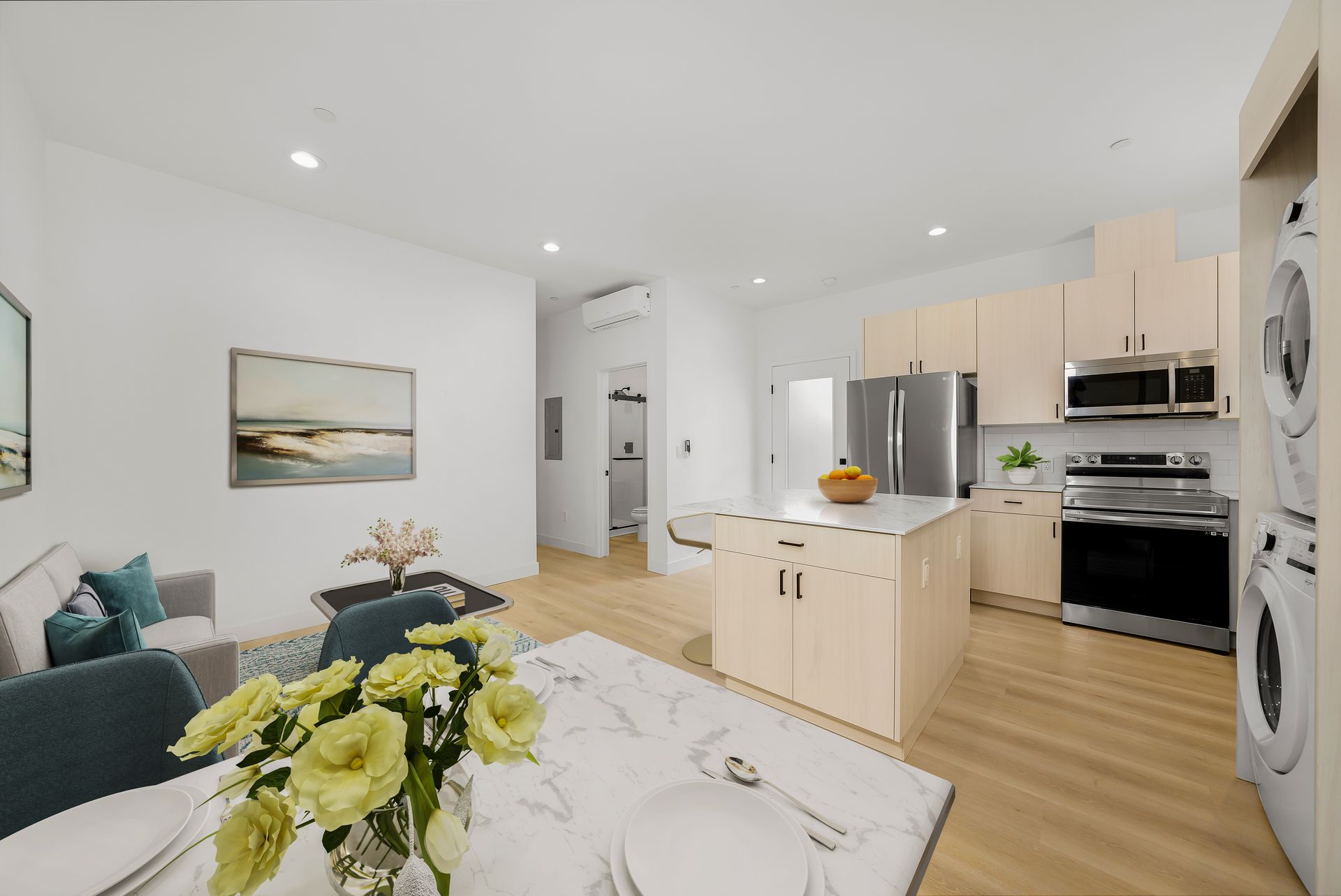 A living room and kitchen in a house with a vase of flowers on the table.