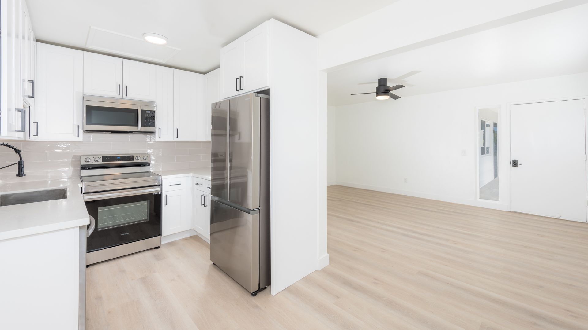 An empty kitchen with stainless steel appliances and white cabinets.