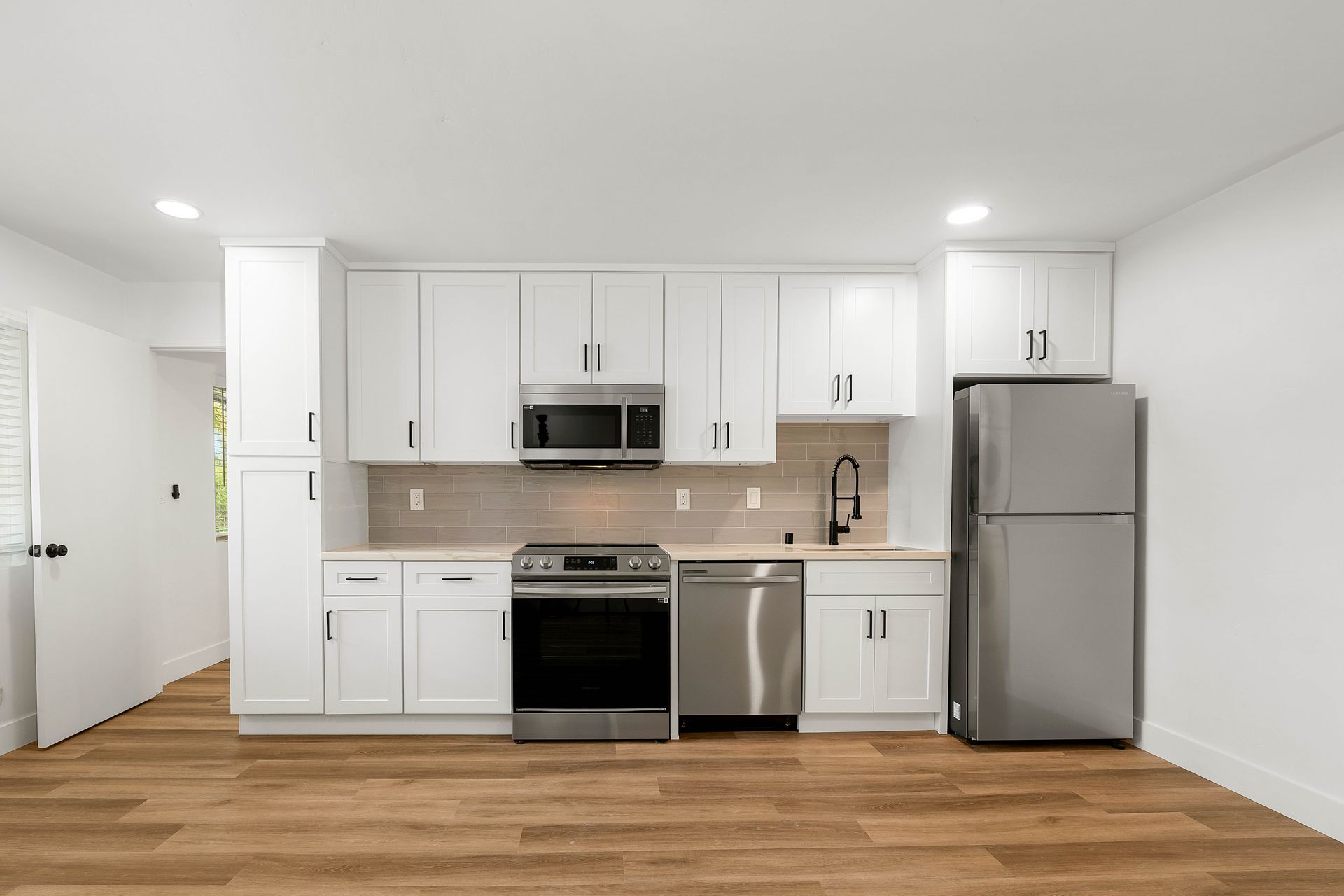 A kitchen with white cabinets , stainless steel appliances , a refrigerator and a microwave.