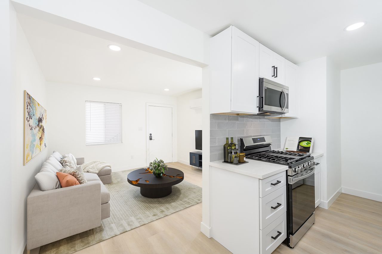 A living room and kitchen in a house with white cabinets and stainless steel appliances.