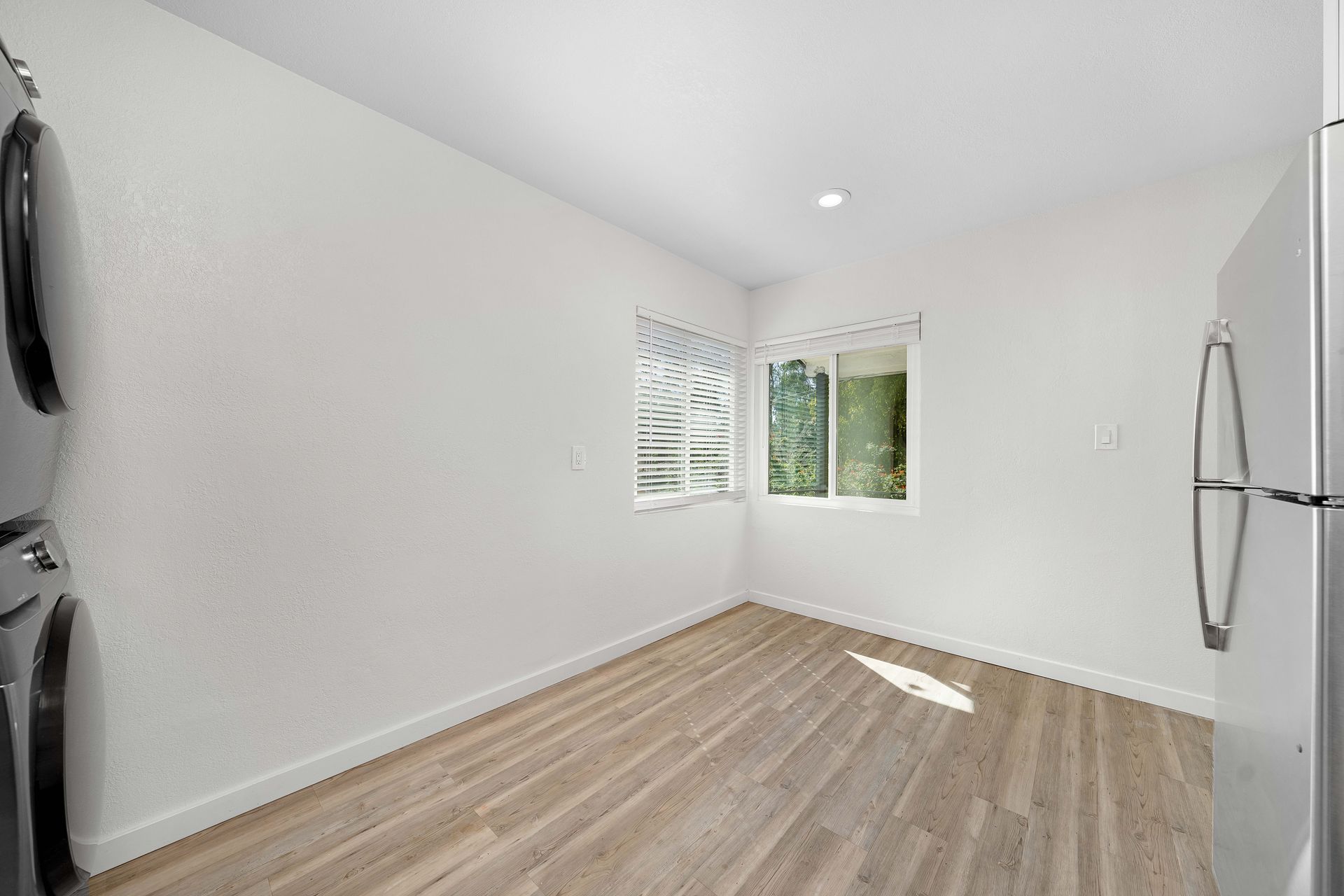 An empty room with a refrigerator , washer and dryer , and a window.
