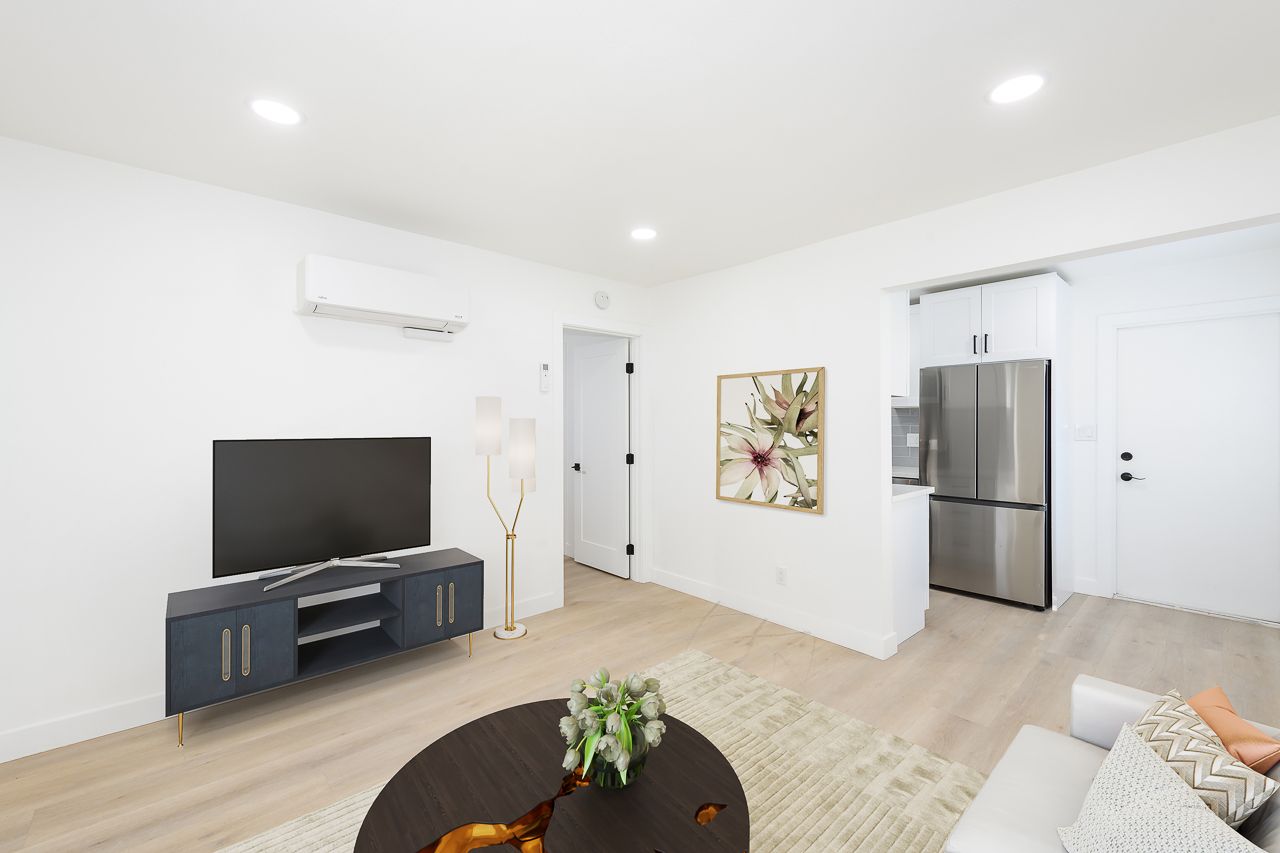 A living room with a couch , television , coffee table and refrigerator.