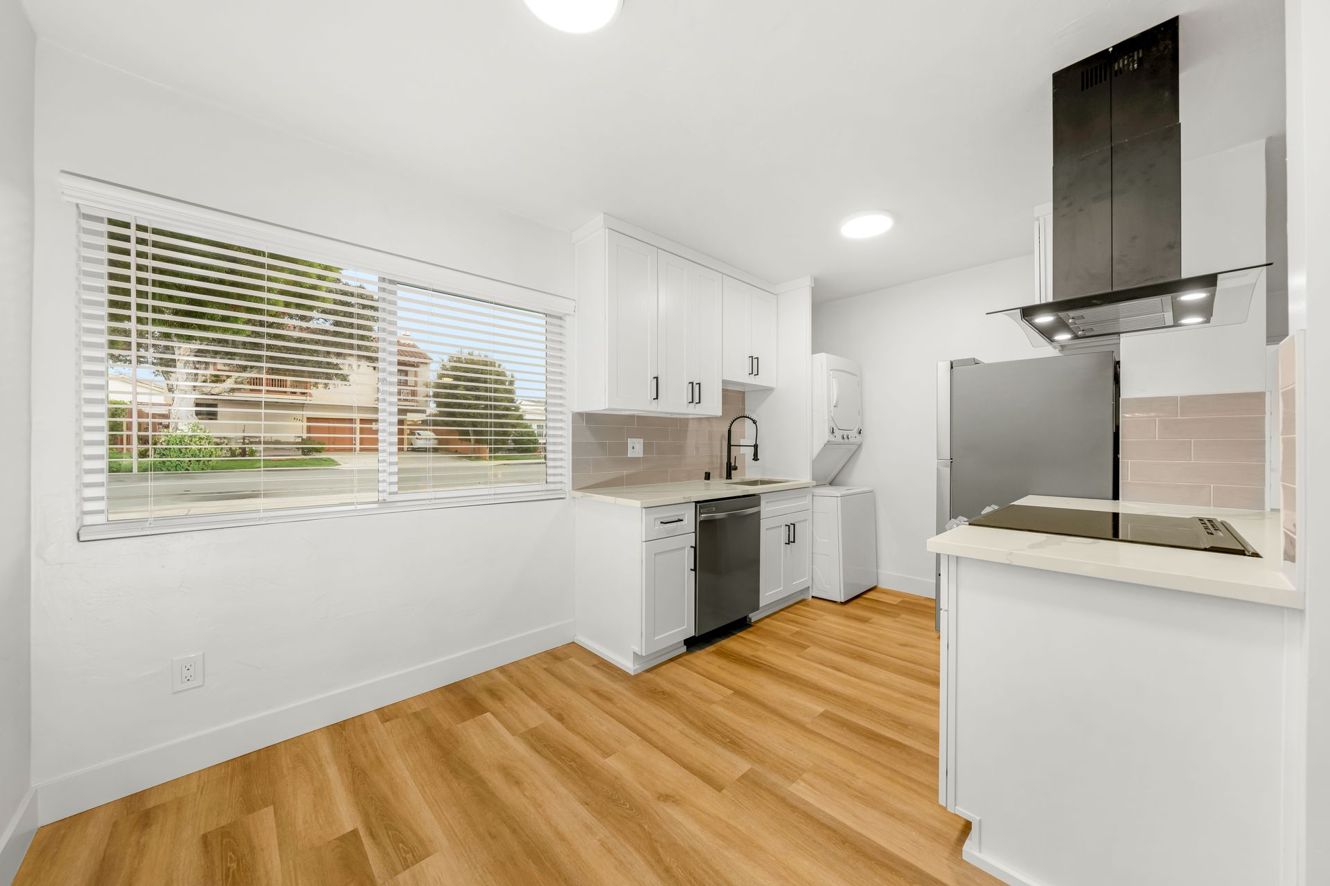 A kitchen with white cabinets and hardwood floors and a large window.