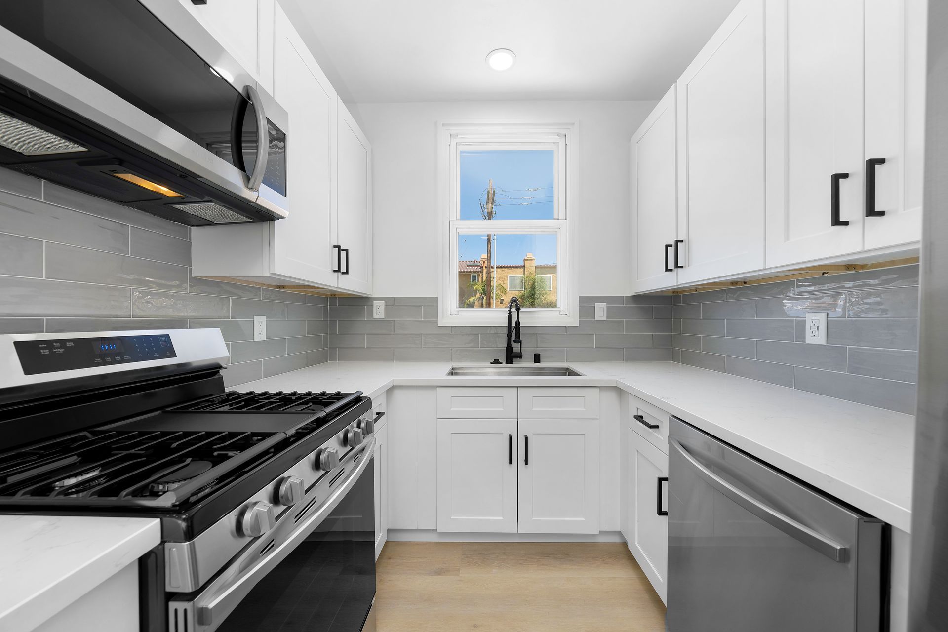 A kitchen with white cabinets , stainless steel appliances , and a window.