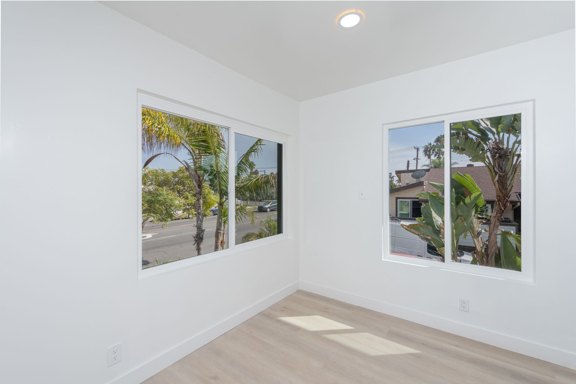 An empty room with two windows and a wooden floor.