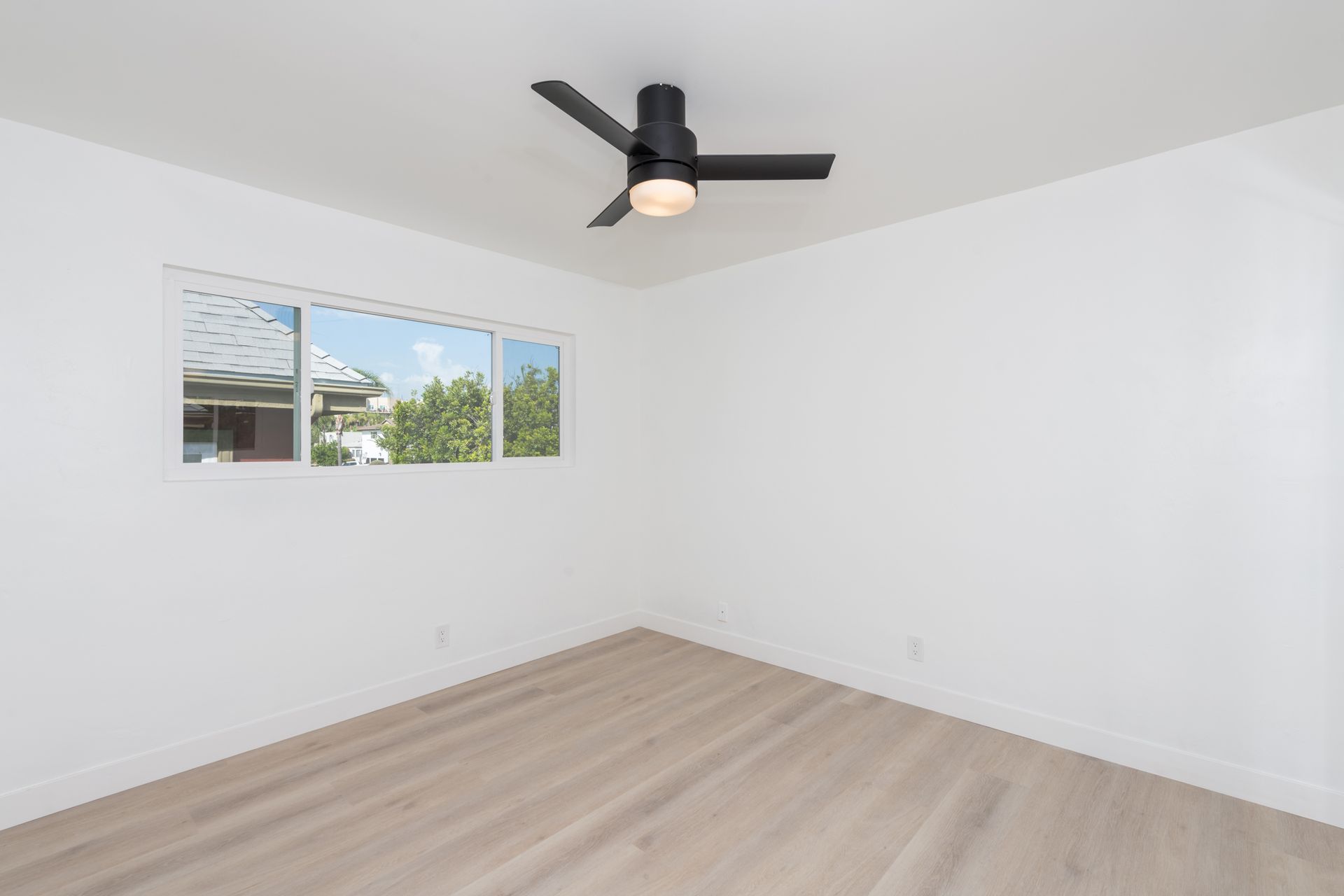 An empty bedroom with a ceiling fan and two windows.