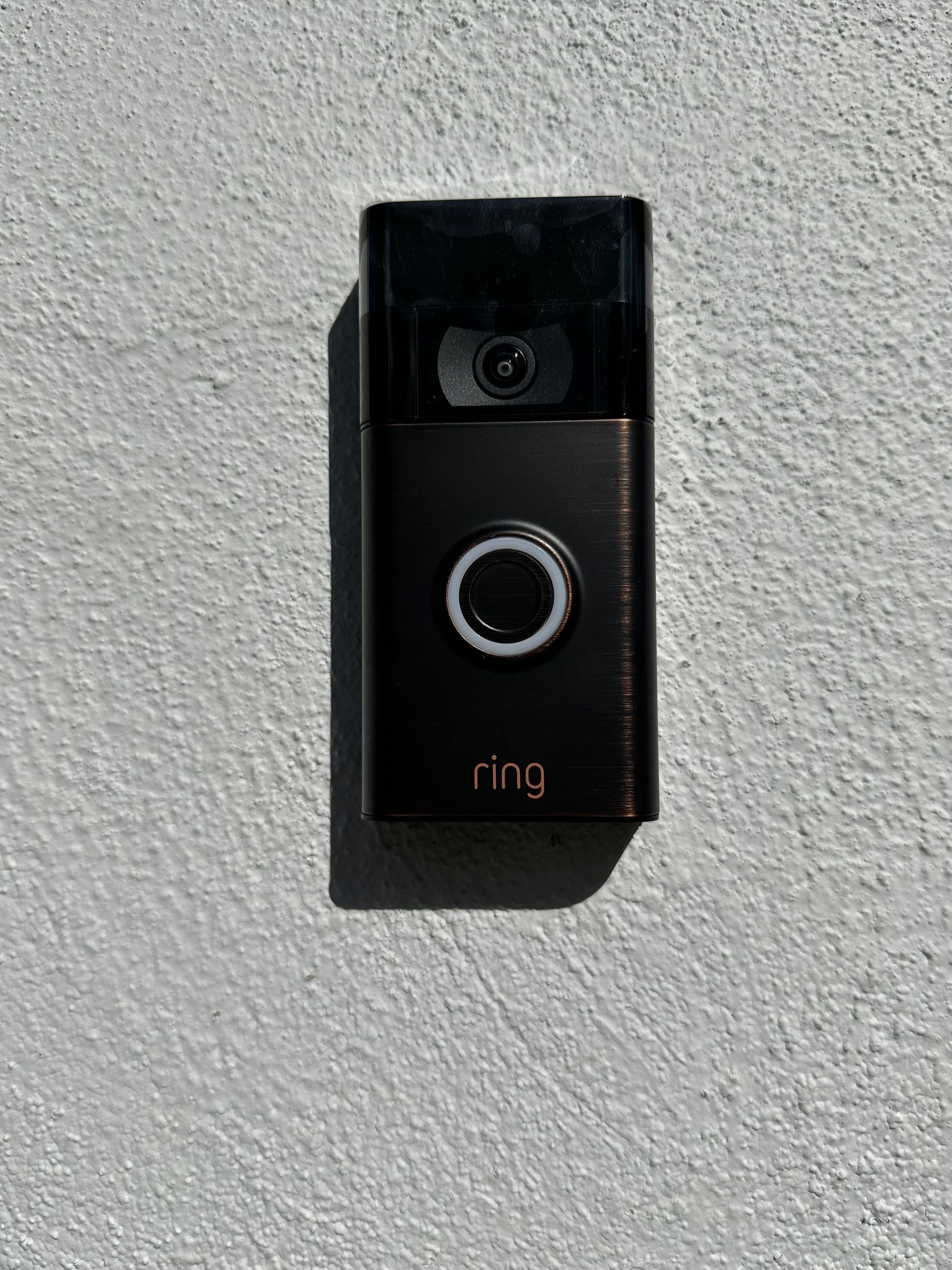 A black ring doorbell is sitting on a white wall.