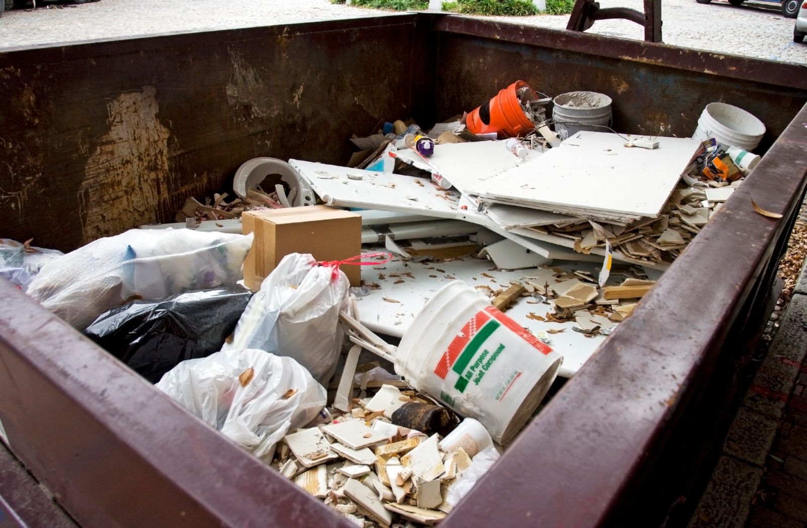 Dumpster filled with construction debris, including drywall, paint cans, and trash bags.