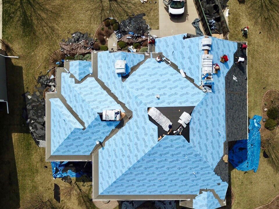 An aerial view of a house with a blue roof being installed.