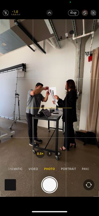 Two people in a studio setting, examining objects on a table. Camera UI in the foreground.